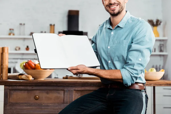 Cropped shot of smiling young man holding blank cookbook in kitchen — Stock Photo