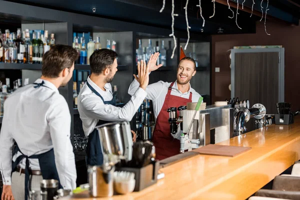 Handsome barmen in aprons high five at workplace — Stock Photo