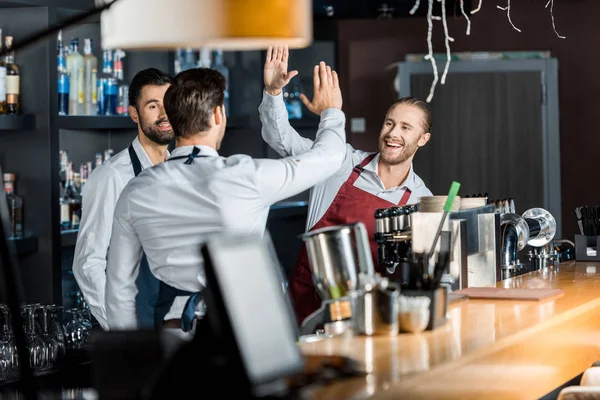 Bel barman sorridente in grembiuli alto cinque sul posto di lavoro — Foto stock