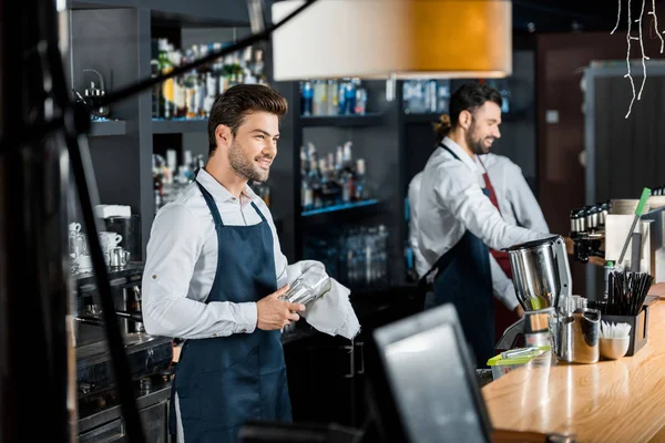 Bonito sorridente barman esfregando até vidro com pano no local de trabalho — Fotografia de Stock