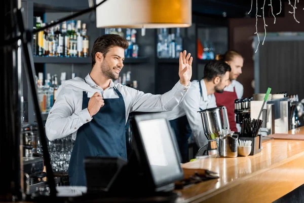 Barman guapo sonriente con saludo de tela en el lugar de trabajo - foto de stock