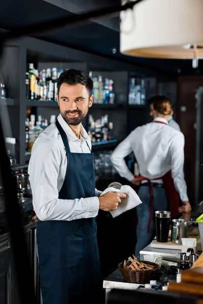 Lächelnder gutaussehender Barkeeper poliert Glas in der Nähe der Theke — Stockfoto