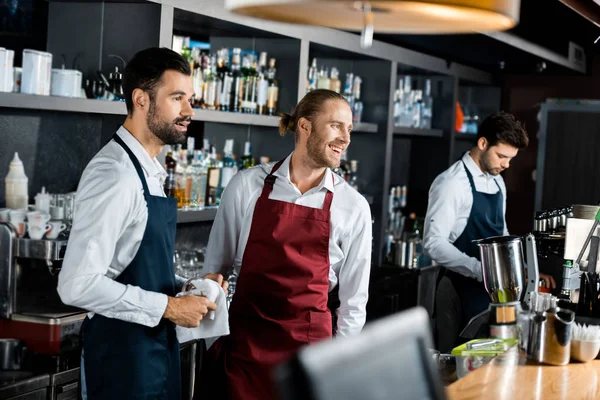 Красивые веселые бармены в фартуках, стоящие на рабочем месте — стоковое фото