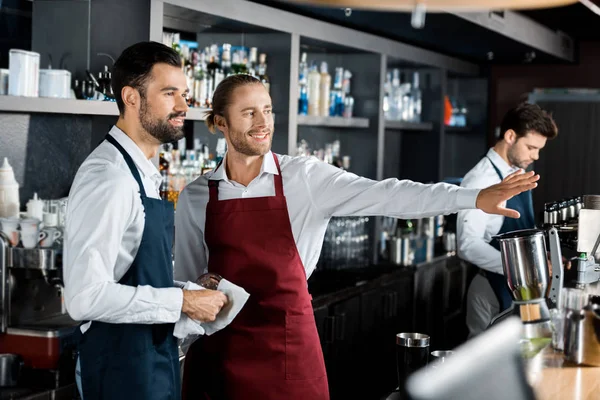 Fröhlich lächelnde Barkeeper gestikulieren am Arbeitsplatz, während Mitarbeiter zur Seite schauen — Stockfoto