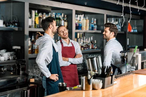Fröhlich gut aussehende Barkeeper in Schürzen unterhalten sich am Arbeitsplatz — Stockfoto