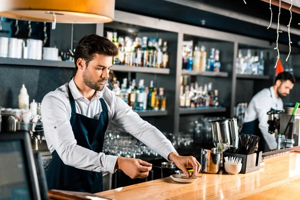 Handsome barista putting sugar sticks and spoon on saucer at counter — Stock Photo