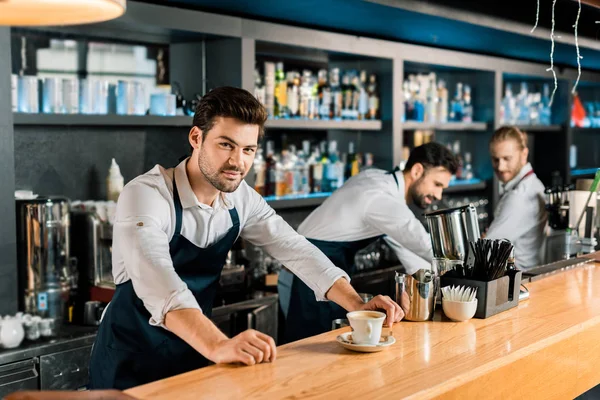 Adulto guapo barista en delantal con café en mostrador de madera — Stock Photo