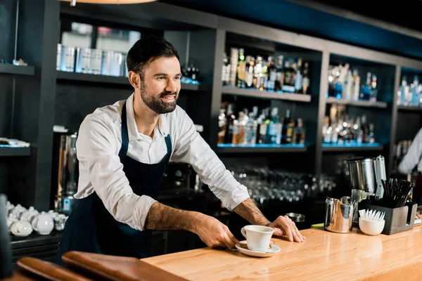 Allegro barista sorridente che serve caffè al bancone in legno — Foto stock