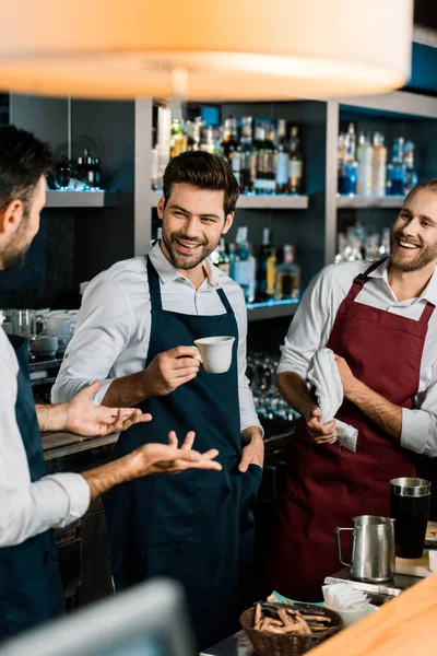 Lächelnder Barmann, der Kaffee trinkt und mit Kollegen am Arbeitsplatz spricht — Stockfoto