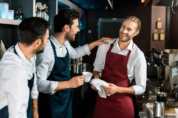 Smiling barman drinking coffee and talking to colleagues at workplace — Stock Photo