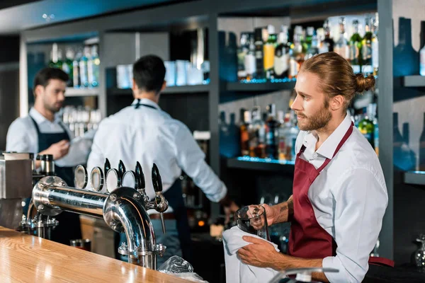 Thoughtful barman polishing glass with cloth at wooden counter — Stock Photo