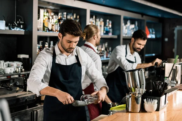 Bel barman in grembiule mettere ghiaccio in vetro con pala di ghiaccio — Foto stock