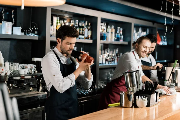 Дорослий бармен в фартусі трясе коктейль в склянці з шейкером — стокове фото