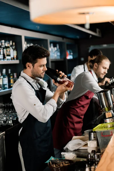 Barman adulto en delantal batiendo cóctel en vaso con agitador - foto de stock