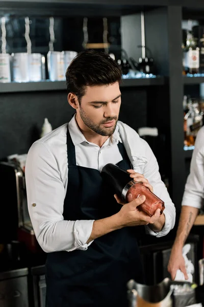 Schöner Barmann in Schürze bereitet Cocktail im Glas mit Shaker zu — Stockfoto