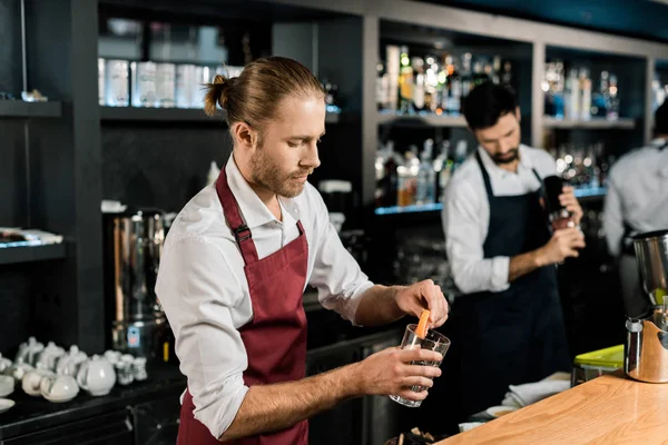 Handsome barman decorating glass for cocktail with grapefruit slice — Stock Photo