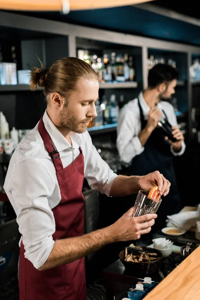 Handsome barman decorating glass for cocktail with grapefruit slice — Stock Photo