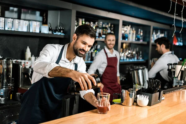 Smiling bartender pouring cocktail in glass at wooden counter — Stock Photo