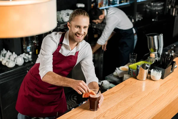 Smiling barman holding cocktail with grapefruit slice at wooden counter — Stock Photo