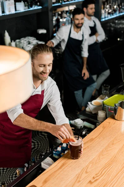 Barman sonriente poner cóctel con rodaja de pomelo y paja en el mostrador de madera - foto de stock