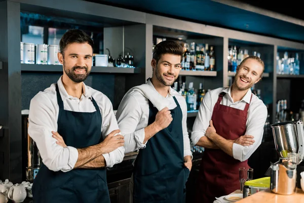 Взрослые бармены в фартуках стоят на рабочем месте со скрещенными руками — стоковое фото