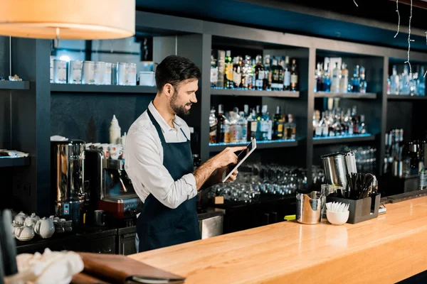 Barmann steht in Schürze und tippt auf digitalem Tablet — Stockfoto