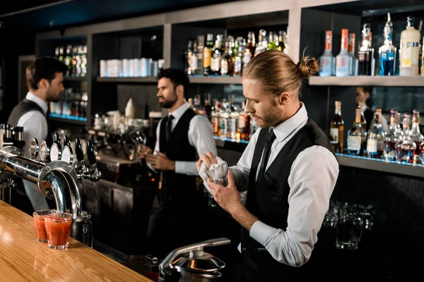 Handsome bartender standing in bar and cleaning glass — Stock Photo