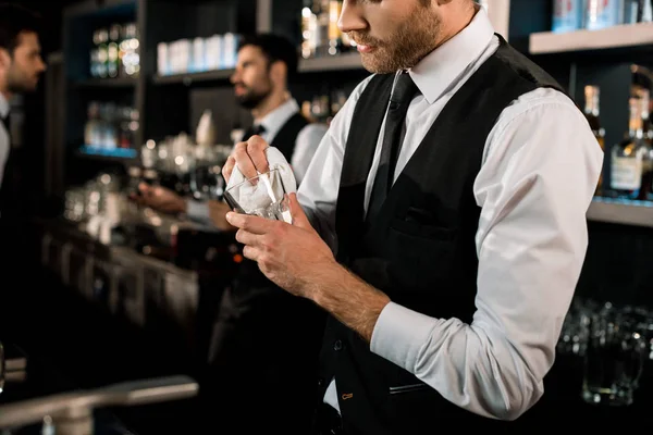 Bartender cleaning glass with white cloth in bar — Stock Photo