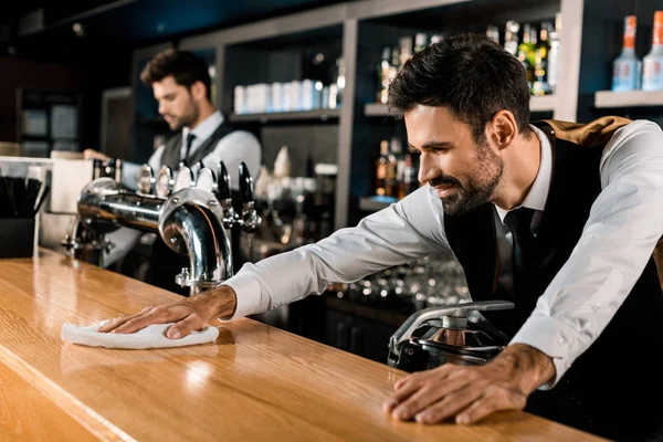 Barman cleaning wooden counter with white cloth — Stock Photo