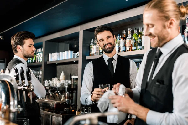 Handsome bartenders smiling in bar and cleaning glasses — Stock Photo