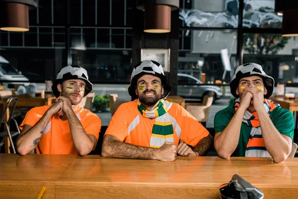 Футбольні фанати дивляться гру, сидячи в капелюхах в барі — стокове фото