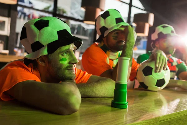 Aficionados al fútbol sentados en sombreros, viendo fútbol en el bar - foto de stock