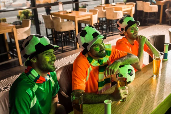 Aficionados al fútbol sosteniendo vasos con cerveza y viendo el partido en el bar - foto de stock