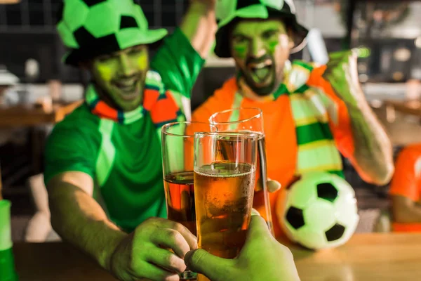 Aficionados al fútbol animando tintineo vasos de cerveza en el bar - foto de stock