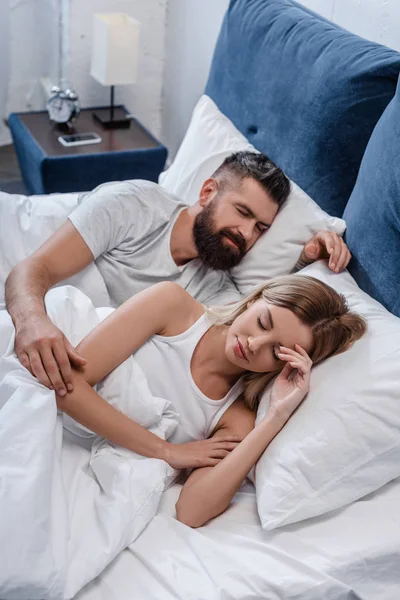 Bearded young man and beautiful girl sleeping in big white bed in morning — Stock Photo