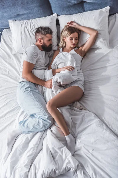 Bärtiger Mann und attraktives Mädchen mit der Hand hinter dem Kopf, die im weißen Bett schläft — Stockfoto