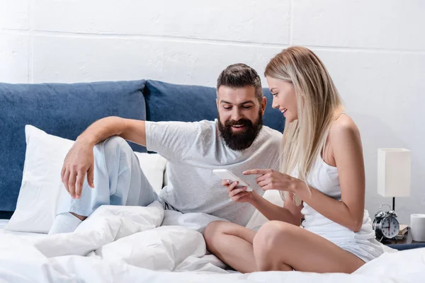 Счастливая влюбленная пара использует смартфон в постели по утрам — стоковое фото