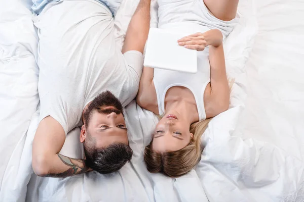Молода пара лежить в ліжку і дивиться на білий цифровий планшет — стокове фото