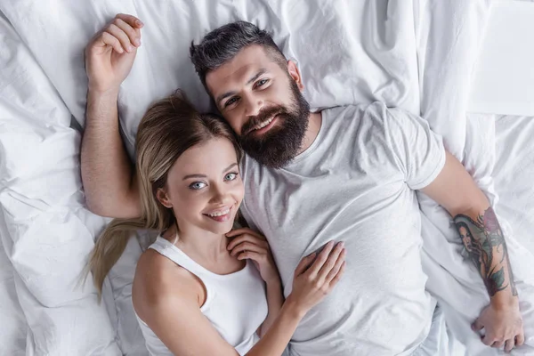 Jovem casal sorrindo deitado na cama e olhando para a câmera — Fotografia de Stock