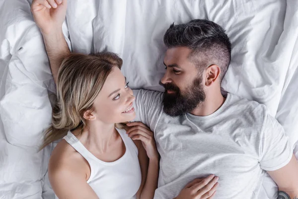 Jovem casal sorrindo deitado na cama e olhando um para o outro — Fotografia de Stock