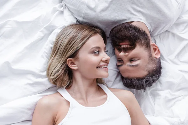 Jovem casal apaixonado mentindo cabeça a cabeça e olhando um para o outro em cobertor branco — Fotografia de Stock