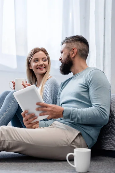 Paar lächelt und sitzt in lässiger Kleidung mit digitalem Tablet — Stockfoto