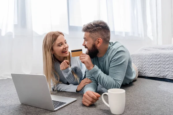 Couple souriant couché sur le sol avec ordinateur portable et carte de crédit — Photo de stock