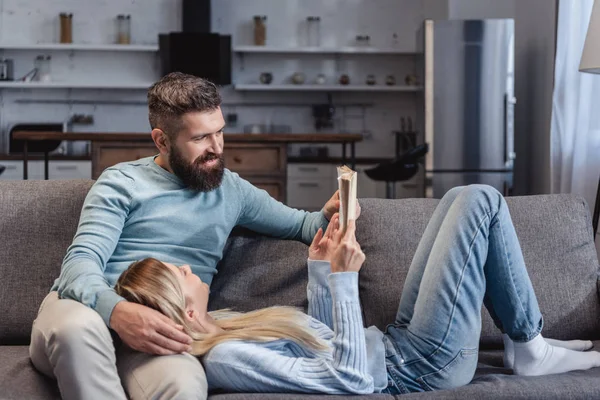 Wife holding book and lying on knees of husband — Stock Photo