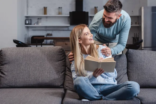 Marido alegre abraçando bela esposa com livro — Fotografia de Stock