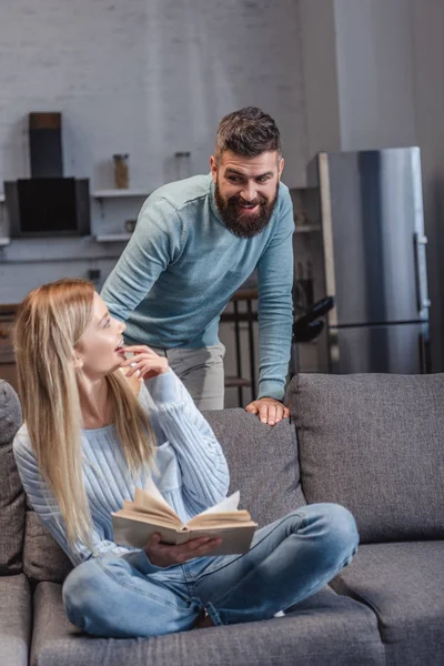 Alegre marido sonriendo a feliz esposa con libro - foto de stock