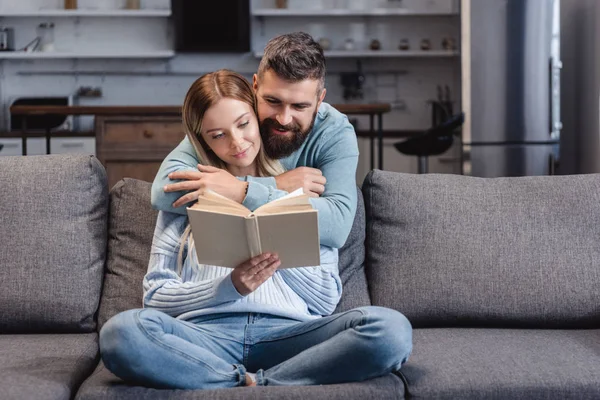 Fröhlicher Ehemann umarmt attraktive Frau mit Buch — Stockfoto