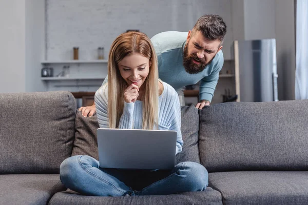 Дружина сидить з ноутбуком на дивані і чоловік дивиться на монітор — Stock Photo