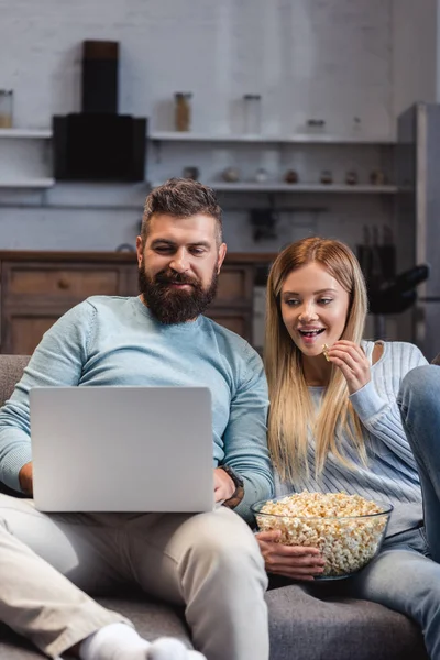 Пара сидящих с попкорном и смотрящих фильм на ноутбуке — стоковое фото