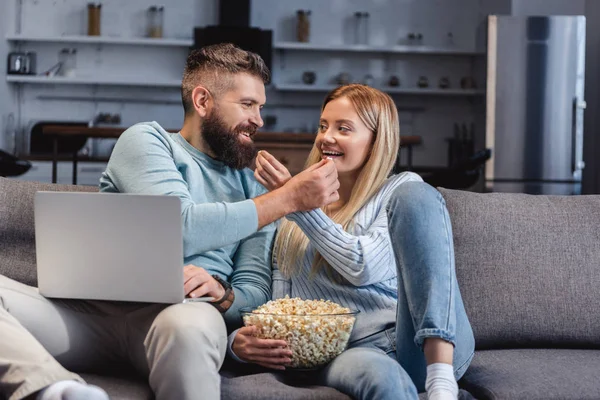 Husband and wife sitting on sofa and sharing food — Stock Photo